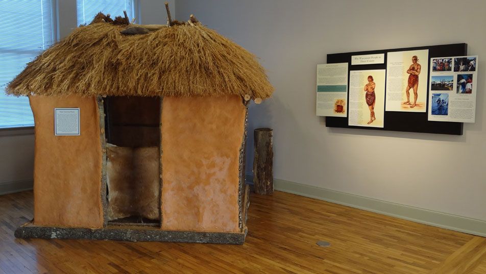 The Native American gallery: a full-size thatched-roof dwelling built of daub and cane, with an interpretive panel on the wall beside it.