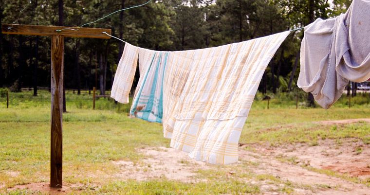 Washing pegged out on a clothesline strung between two timber posts, drying in the sun beside the farm yard.
