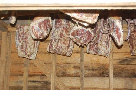 Cured hams and shoulders hanging in rows from the rafters of the smokehouse.