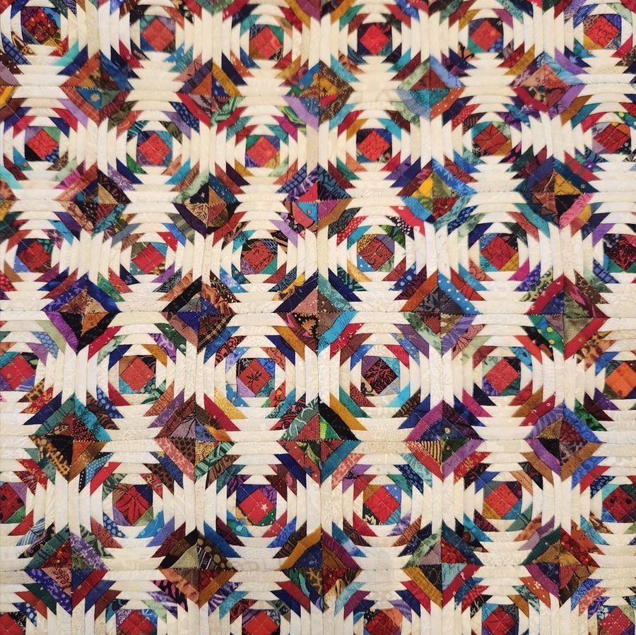 A close view of a pieced quilt in a repeating pineapple block pattern, in reds, blues and cream.